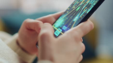 close up on a person hands playing an arcade video game on a vertically held smartphone at home living room. feminine hands tapping the mobile phone screen with a colorful game over the internet.