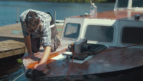 joven carpintero limpiando el polvo de la proa del barco de madera lijada antes de barnizar