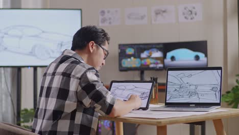 side view of asian male stretching while drawing new car design concept on a tablet in the studio with tv and computers display 3d electric car model