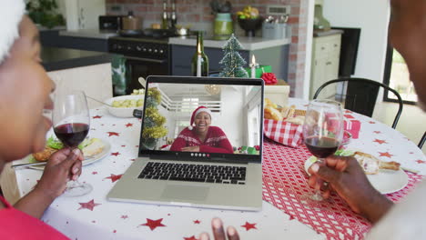 pareja afroamericana con vino usando computadora portátil para una videollamada de navidad con una mujer en la pantalla