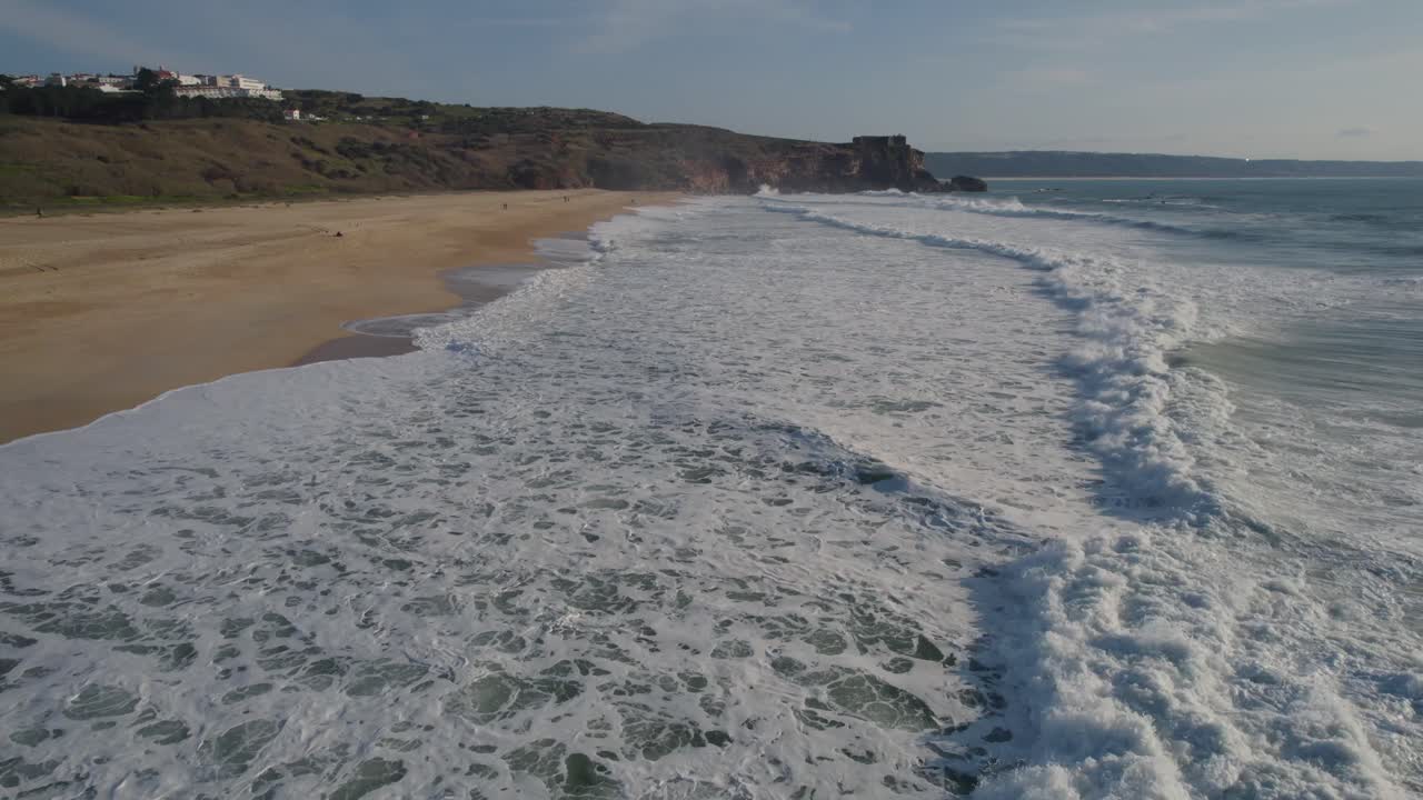las olas chocan suavemente contra la orilla y envían una ráfaga de burbujas y espuma a través de la arena en una playa en nazare