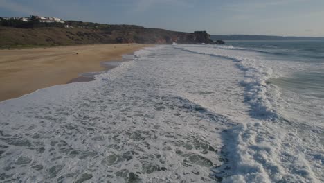 Olas-Rompiendo-Suavemente-En-La-Orilla-Y-Enviando-Una-Ráfaga-De-Burbujas-Y-Espuma-A-Través-De-La-Arena-En-Una-Playa-De-Nazare