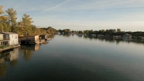 las imágenes de drones capturan un río tranquilo en europa central alineado con casas flotantes y árboles de otoño.