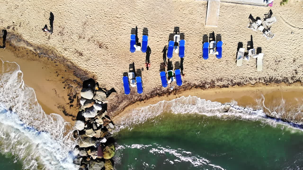 Aerial drone view of the Aegean sea coast in Nikiti, Greece. Beach with waves of the sea, sunbeds with resting people and terrace top view
