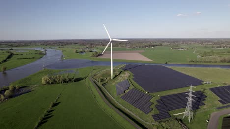 Der-Twentekanal-Trifft-Auf-Das-Tal-Des-Flusses-Ijssel-Und-Nähert-Sich-Einer-Windmühle-Mit-Rotierenden-Rotorblättern,-Die-über-Einem-Feld-Mit-Solarmodulen-Aufragen