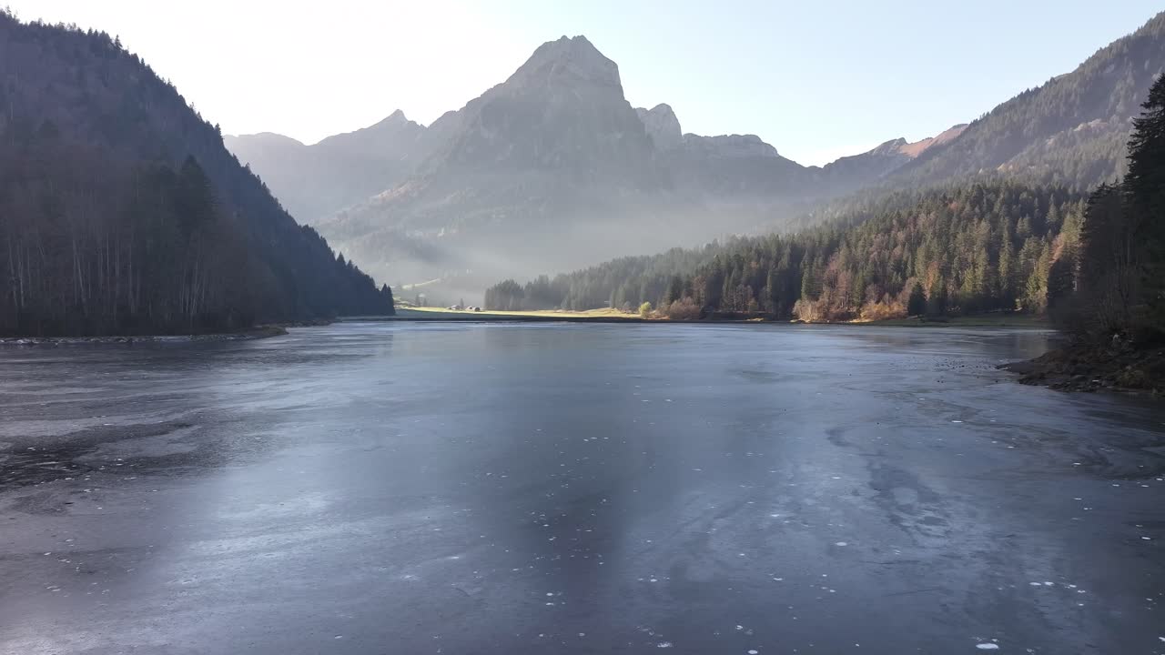 Frozen Obersee with surrounding forests and mountain reflections under mist in Näfels, Switzerland
