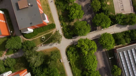 city street, sidewalk, greenery and apartment building rooftops with parking lot, aerial top down view