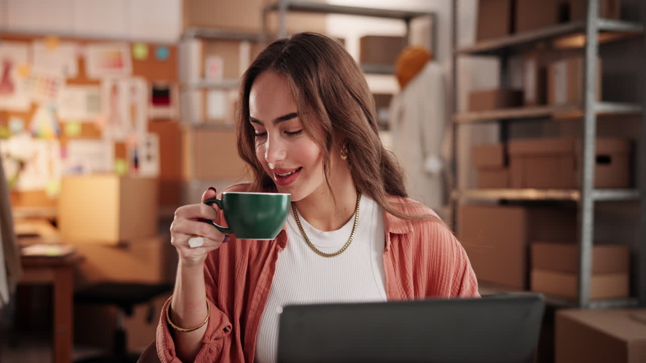 Giovane donna che si gode un caffè mentre lavora al laptop in ufficio