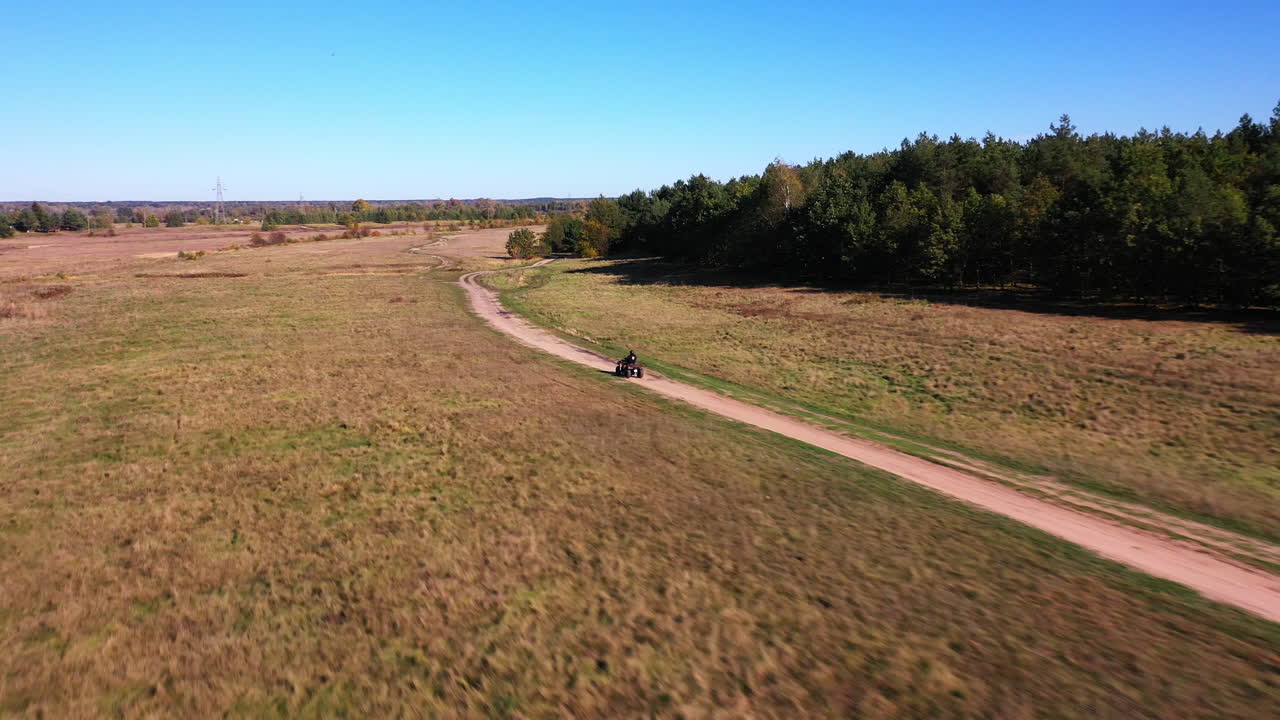 Wide tracking drone shot of quad riding in the nature in the day