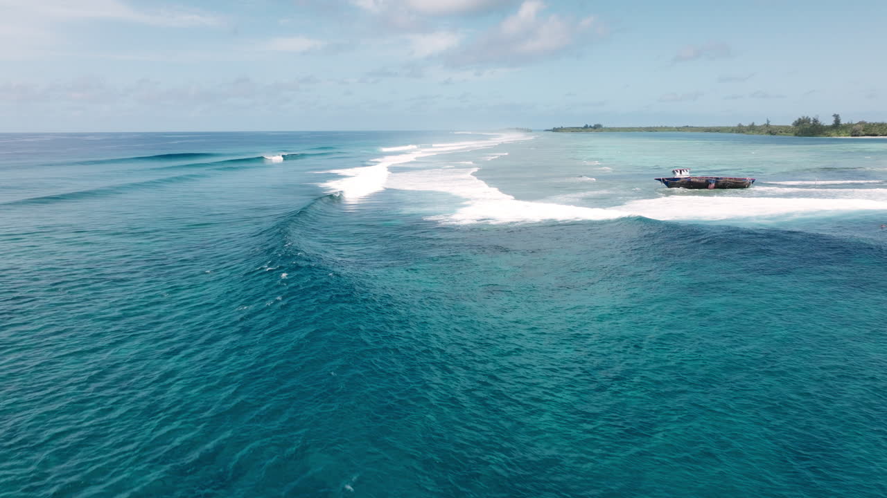 Panoramic aerial approach of Maldives atoll with reef edge meeting deep open ocean as waves build and crash around shipwrecked boat