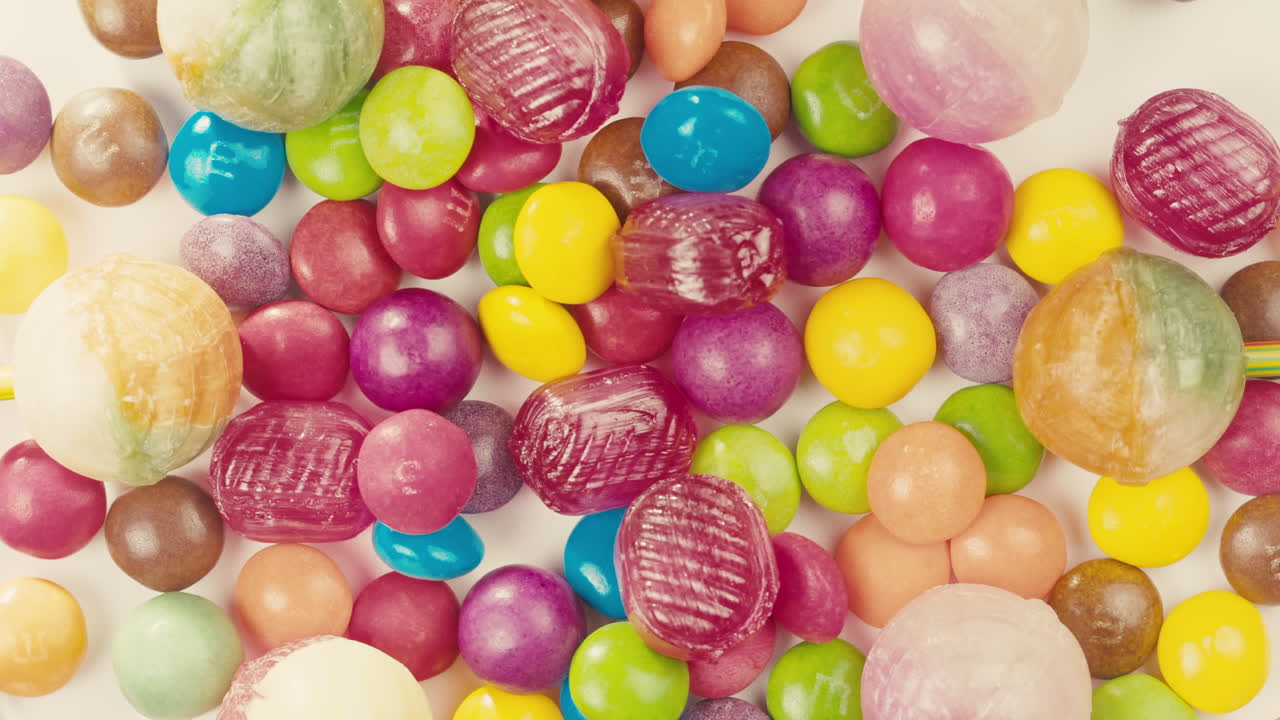 Colorful dragee candies,lollipops with glitter sprinkles on white background,move in circle,top view close-up. Summer bright texture studio shot for store,supermarket. Children's sweets made of sugar.