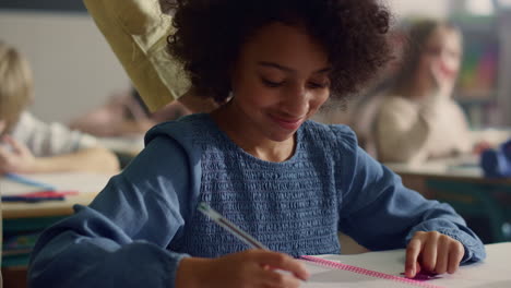 girl talking with teacher in classroom. smiling schoolgirl writing in notebook