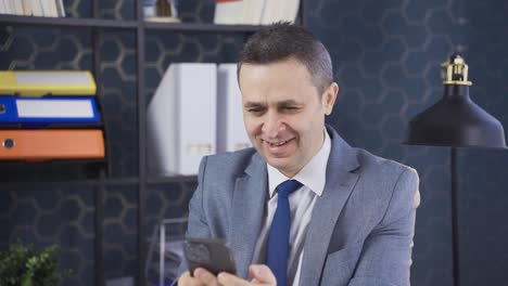 Smiling-mature-businessman-holding-smartphone-in-office.