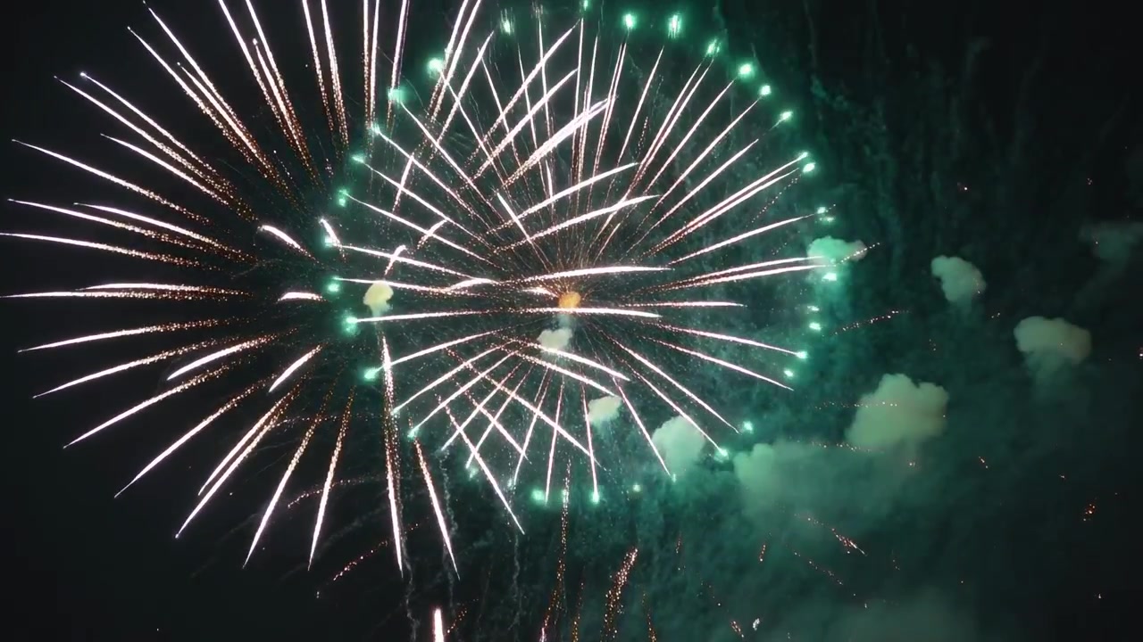 Bursting aerial shells after launch during show forming rings over night sky with sparks and smoke