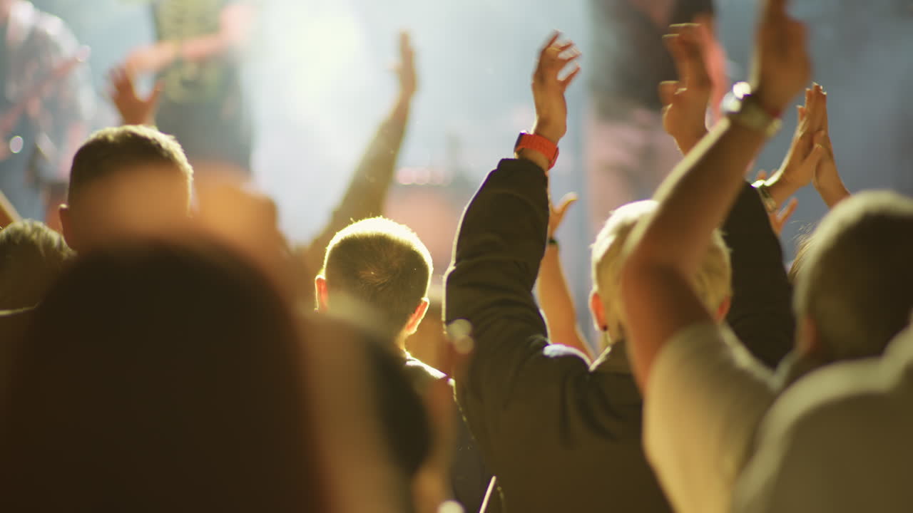Concert crowd with raised hand and wristband in warm stage light