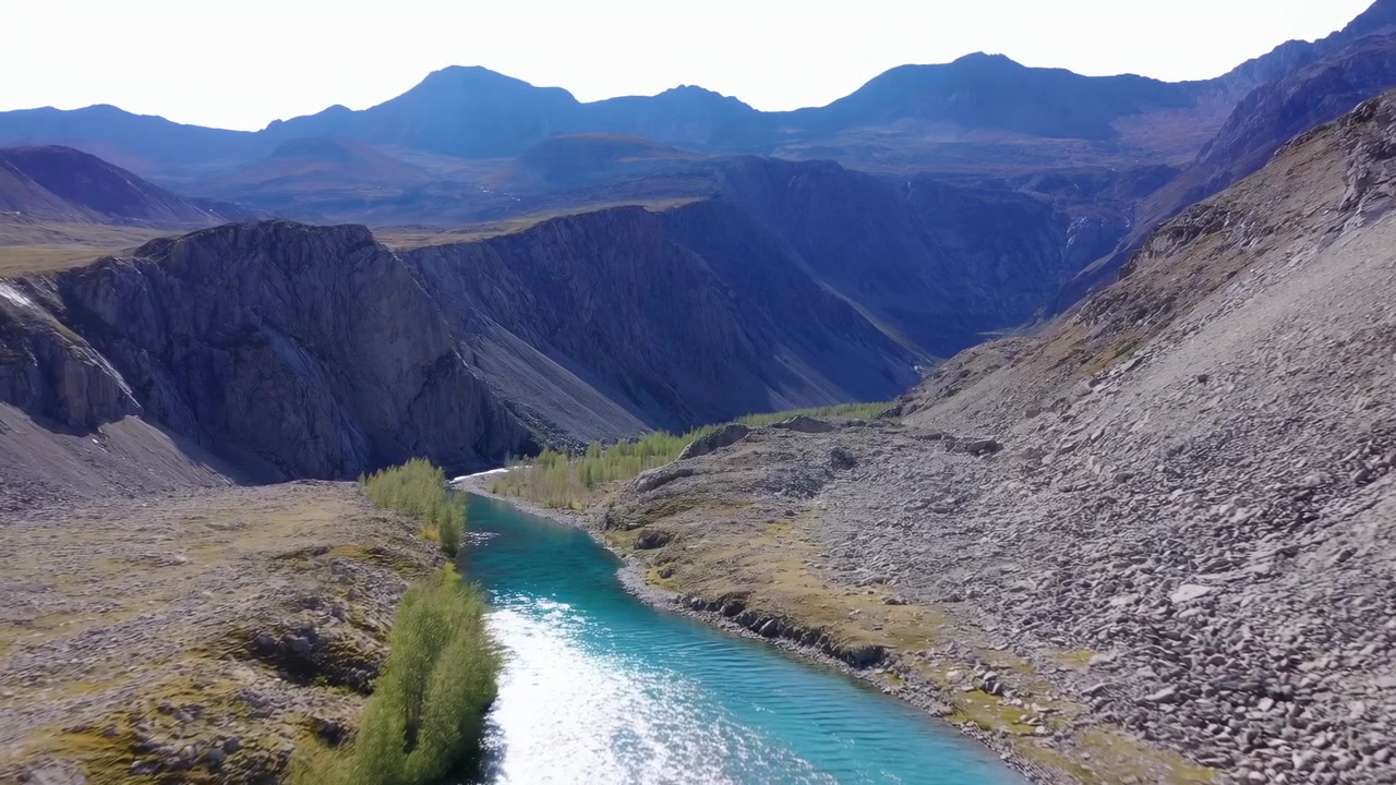 Türkisfarbener Fluss schlängelt sich durch Gebirgstal, Drohnenperspektive zeigt schroffe Felsen und Geröllhänge