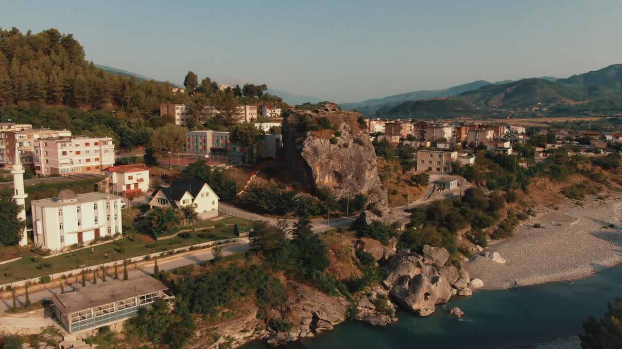 Arnavutluk'taki Permet'in, altın saatte vadiden akan Vjosa nehri ve şehir kayasını içeren havadan görünümü.