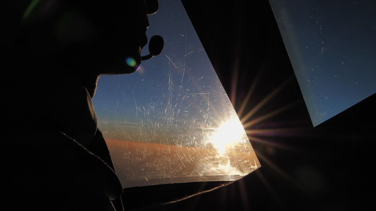 cerca de un piloto masculino en la cabina del avión hablando por radio en cámara lenta retroiluminada por el sol poniente