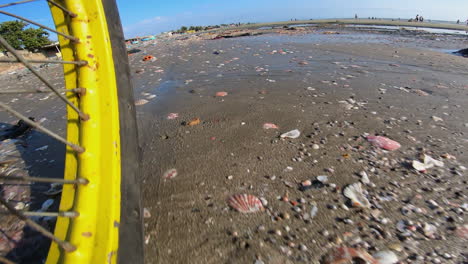 primer plano de una rueda de bicicleta amarilla en una playa de arena llena de basura en vietnam