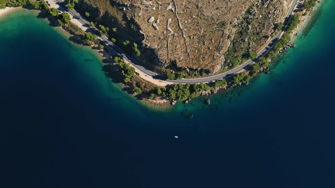 Aerial dolly shot drone footage of cars driving on a coastal road on a peninsula along a beautiful bay with crystal clear water