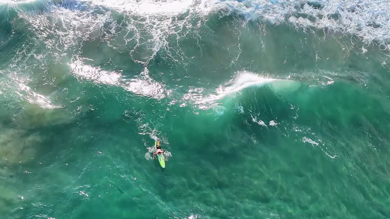 A lone surfer skillfully maneuvers through vibrant green waves from an aerial perspective.