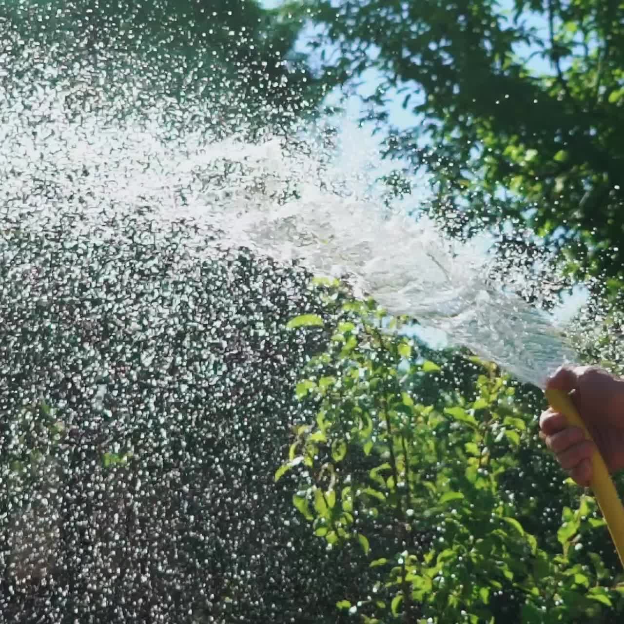 Stream of water spraying from garden hose close-up. Watering the green grass. Slow motion.
