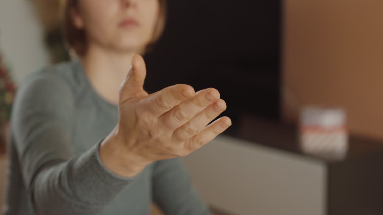 Primo piano di una donna seduta in casa che fa un gesto con la mano per chiedere denaro: concetto di finanza, pagamento, richiesta o frustrazione economica