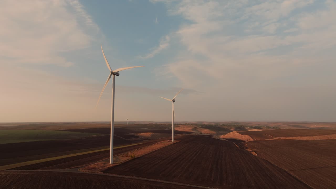 il drone di monitoraggio mostra due mulini a vento in funzione situati nel cuore di ampi campi agricoli, cielo blu, luce solare