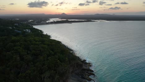 drone footage filmed in noosa of a forest overlooking a pristine beach with clear blue green water