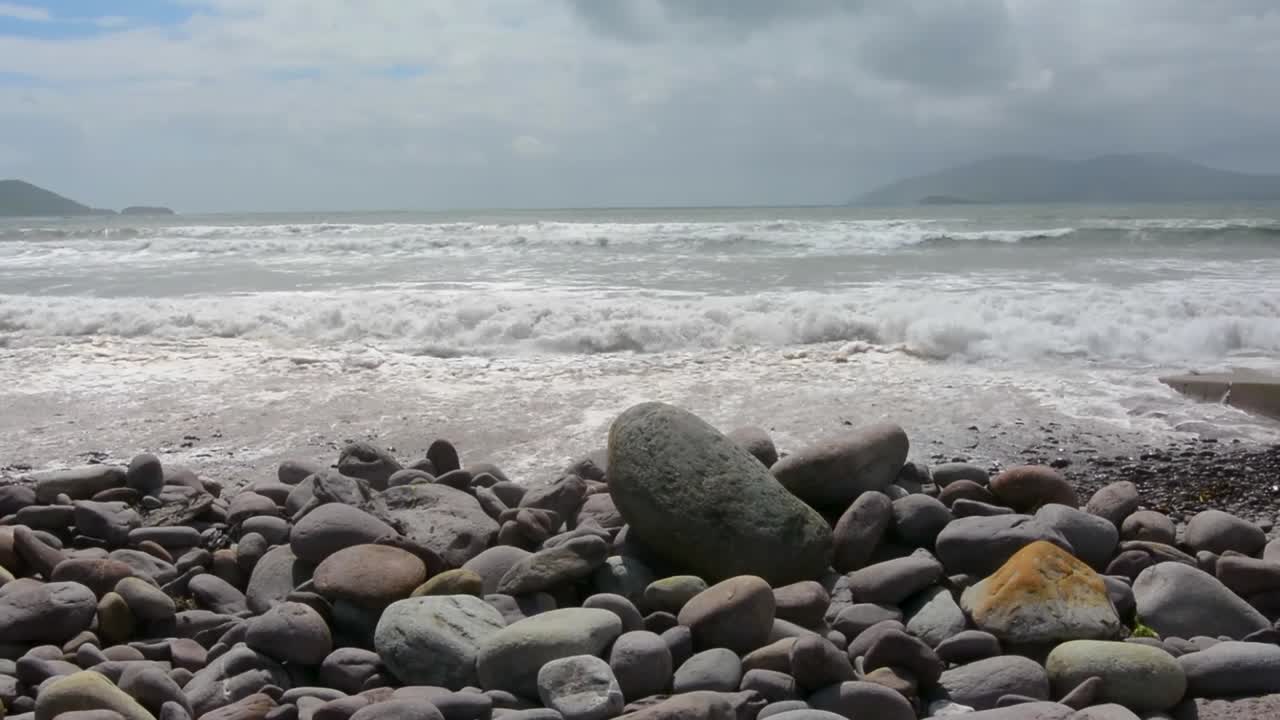 해변 중간 샷에 흐린 하늘과 부드러운 회색 바위를 때리는 평화로운 파도