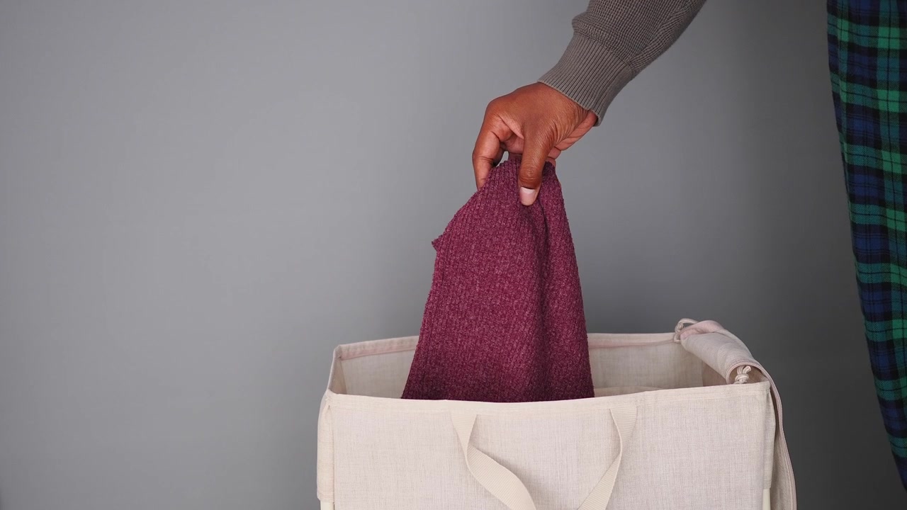 Person Dropping a Maroon Sweater into a Laundry Basket