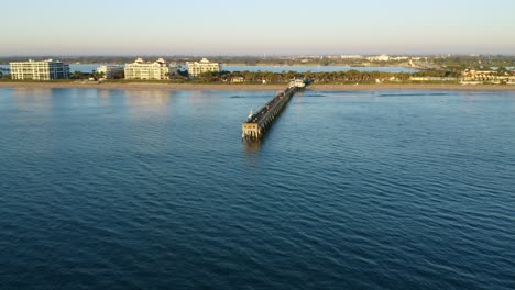 Point-of-Interest-Drohnenaufnahme-In-Florida,-Die-Sich-Bei-Sonnenaufgang-Um-Den-Lake-Worth-Pier-Dreht-Und-Nach-Westen-In-Richtung-Strand-Und-Häuser-Am-Wasser-Blickt