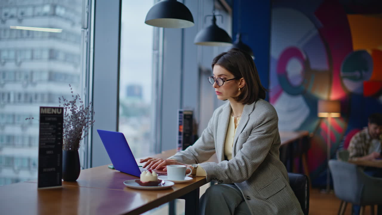 Imprenditrice che digita al computer in una caffetteria, riflettendo su una risposta. Scrittore che crea un libro