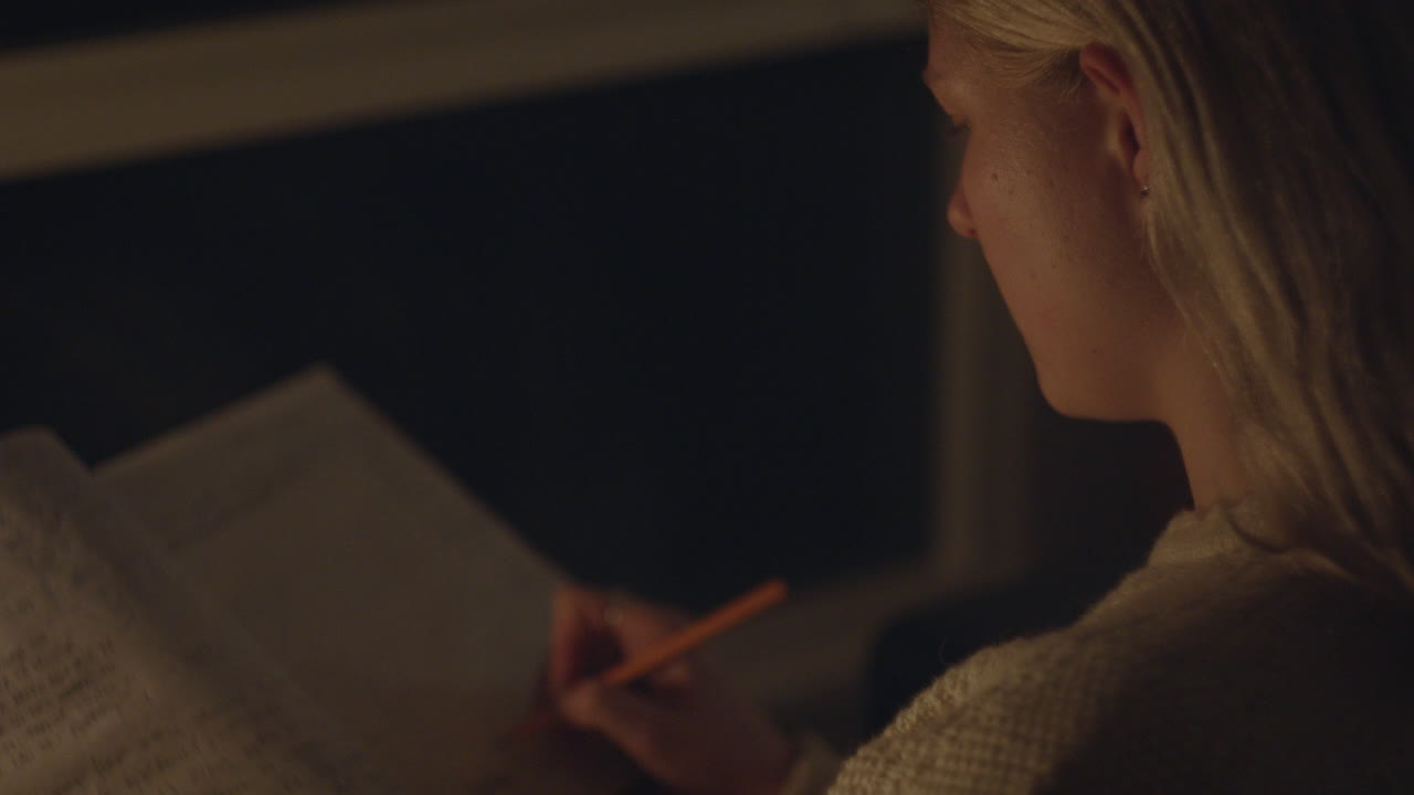 A young woman writes in her journal, her face softly lit by candlelight, immersed in deep reflection and personal expression.