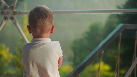 little child looks at nature through transparent wall. calm preschooler rests alone in comfortable tent with tubular frame on blurred background slow motion backside view