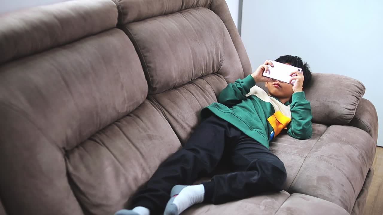 Young asian boy engrossed in mobile game on comfy couch