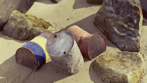 weathered barrels on sandy beach near rocky formations during daylight