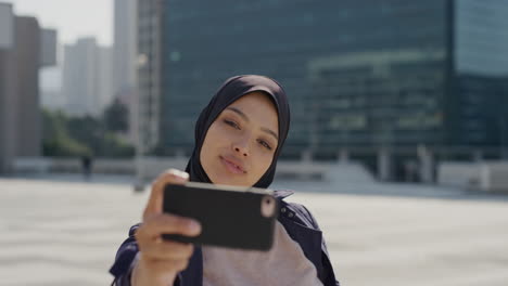 Porträt-Einer-Glücklichen-Jungen-Muslimischen-Frau,-Die-Mit-Ihrem-Smartphone-Ein-Selfie-Foto-Macht-Und-In-Der-Stadt-Gesichter-Macht-Und-Einen-Unabhängigen-Urbanen-Lebensstil-Mit-Hijab-Kopftuch-Genießt