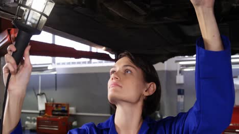 mecánica examinando el coche usando una linterna