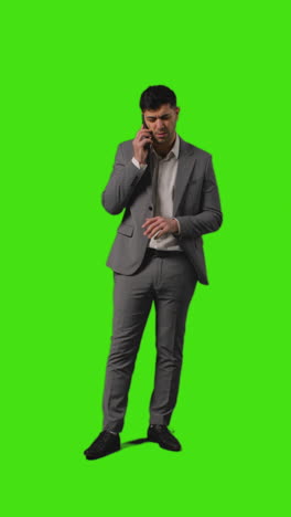 Vertical-Video-Full-Length-Shot-Of-Businessman-Talking-On-Mobile-Phone-Against-Green-Screen-Background