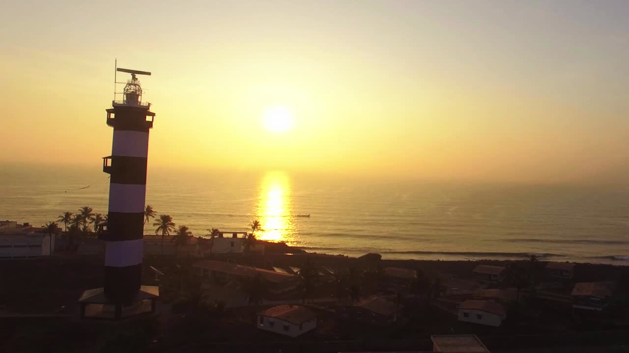 일출과 보트가 태양 광선을 가로지르는 해변의 뒷마당이 있는 등대 실호트를 향해 전진하는 드론 샷