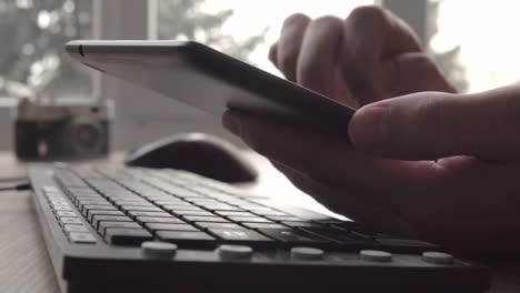 close up on hands of young man using tablet while sitting computer keyboard and mouse. freelancer photographer working and using tablet for communication with clients.