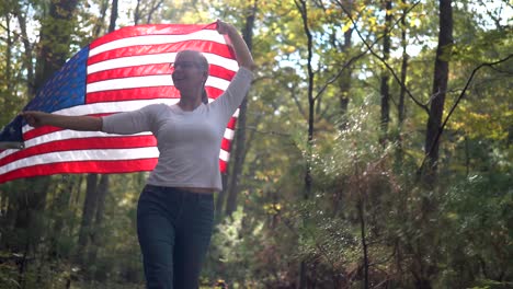 backlit, pretty blonde woman walking through a forest holding a flag up in the air behind her