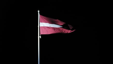 latvian national flag waves dramatically in night sky, strong light create focus