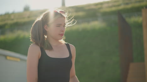 woman closes brown-covered book, taking a deep breath as sunlight shines on her, the wind gently blows her hair, with a serene greenery and wooden structure in the blurred background