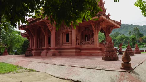 red buddhist temple surrounded by green trees in thailand