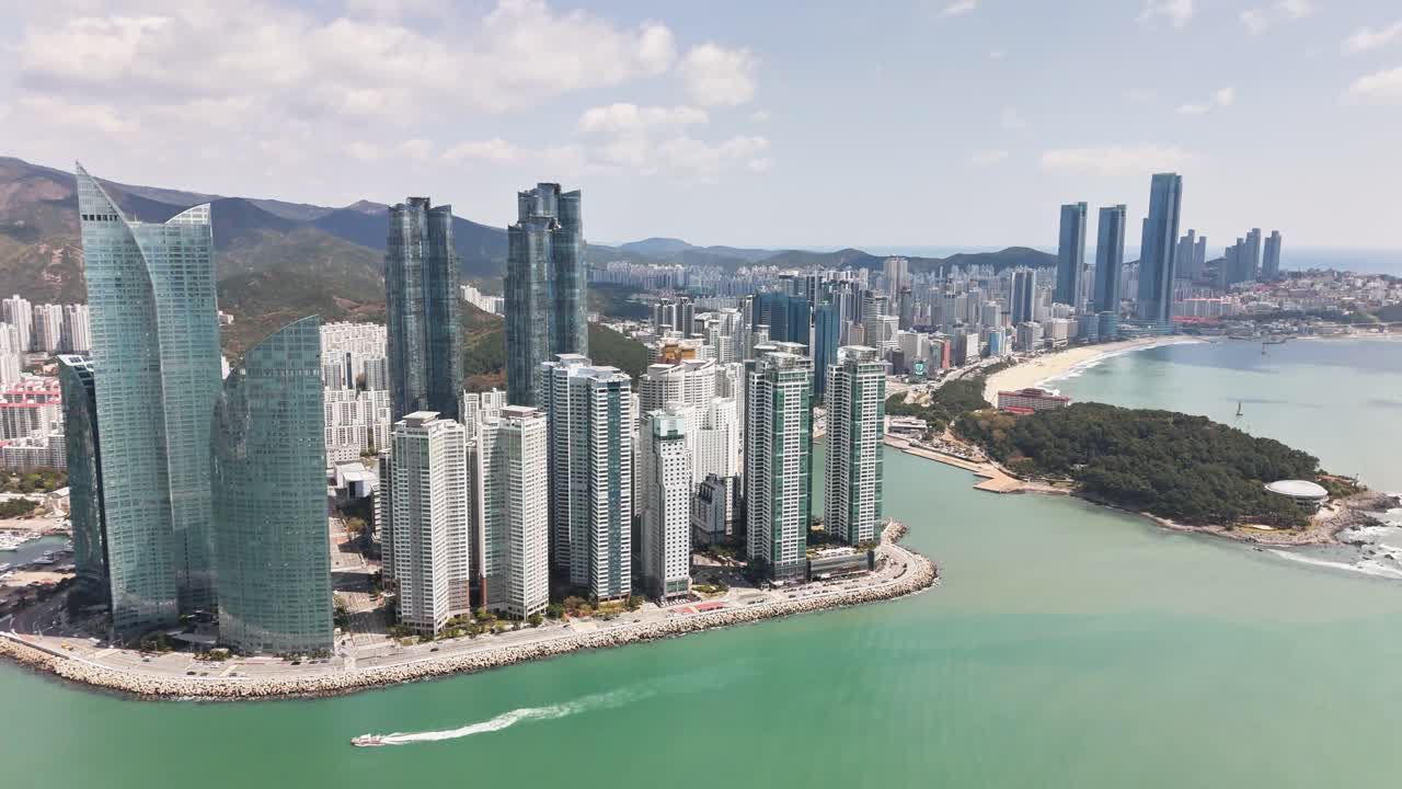 Aerial panorama capturing Busan's contemporary skyscrapers towering over pristine coastline, revealing harmonious blend of urban architecture and natural landscape in South Korean metropolis