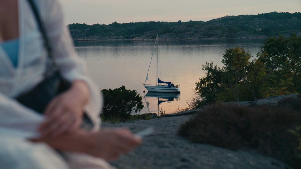 Tranquilla serata estiva scandinava con acqua calma, una barca a vela ancorata e una donna che si gode la pacifica atmosfera costiera