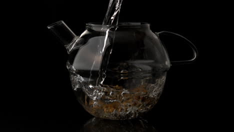 water pouring into glass teapot over loose herbal tea