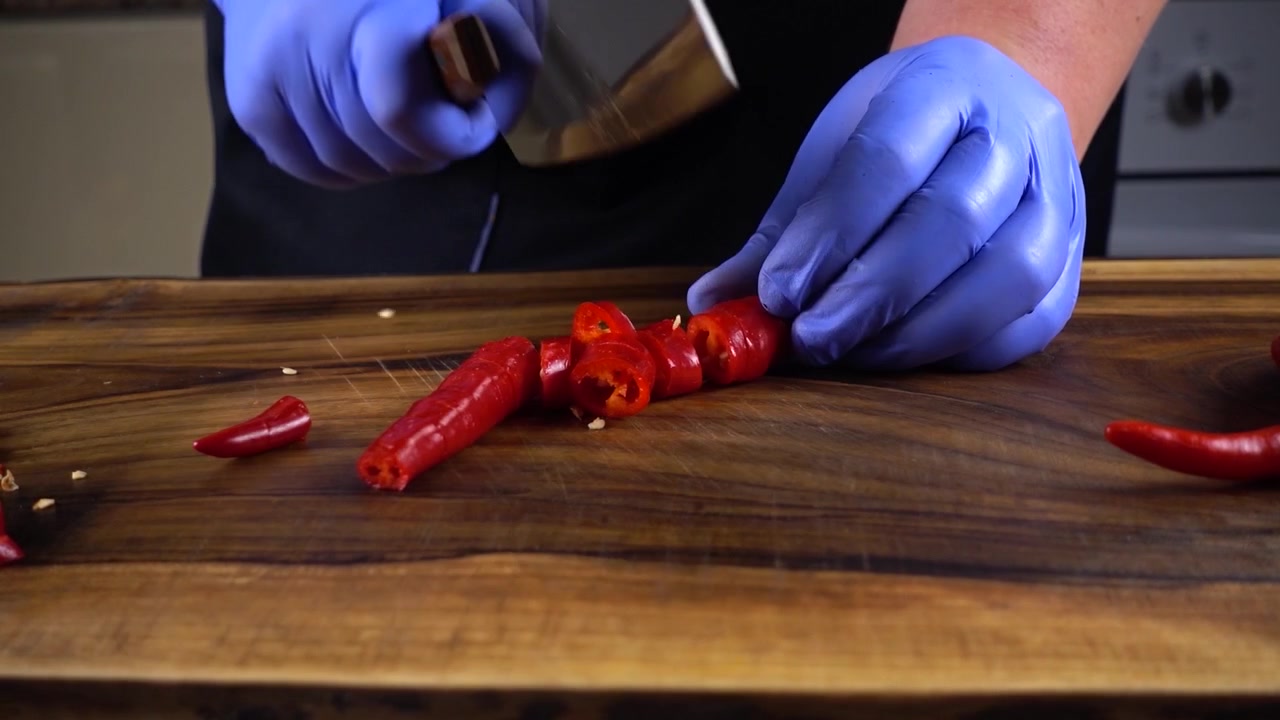The cook cuts chilli pepper on a cutting board.